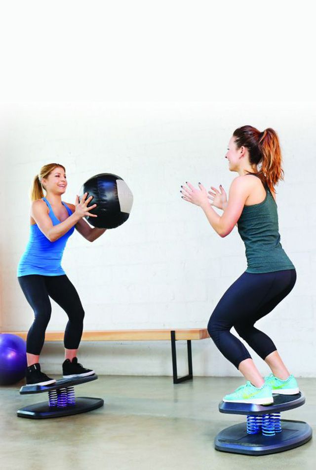 Two women play catch with a medicine ball on StrongBoard Balance Boards to burn more calories